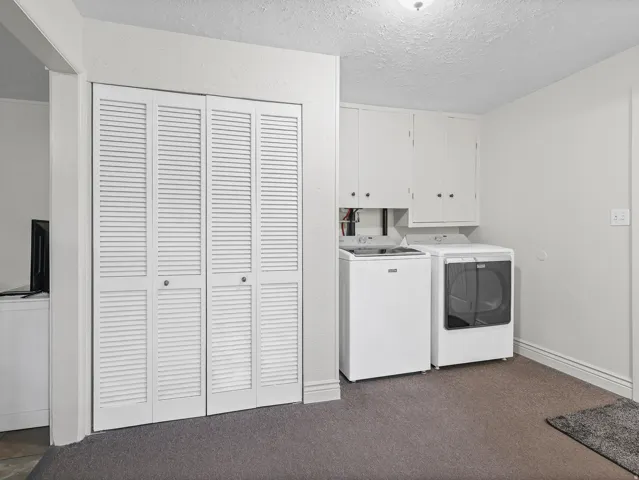 Utility area featuring white bi-fold louvered doors, built-in upper cabinetry, and carpet flooring