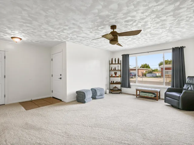 Expansive carpeted living area with a large window and a ceiling fan