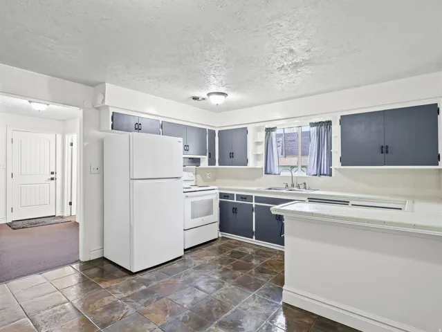 Kitchen featuring tile flooring, white appliances, dark cabinetry, and a double basin sink