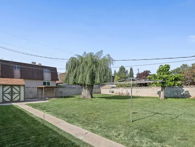 Expansive grassy yard with mature trees, a concrete pathway, and a storage shed