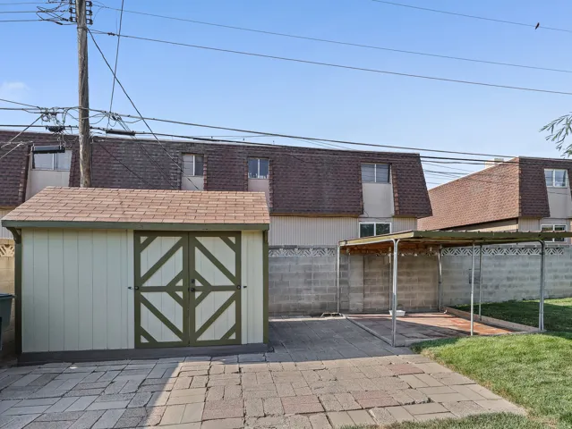 Detached storage shed with decorative doors, paved patio, and covered carport structure
