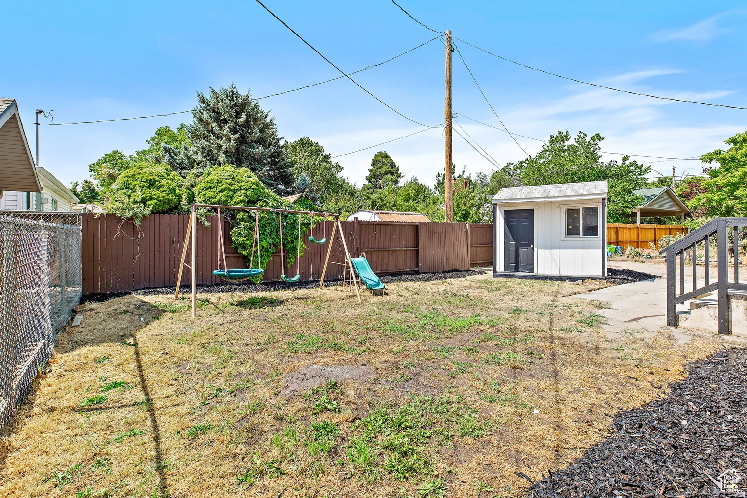 Fenced backyard featuring a storage shed, wooden privacy fencing, chain link fencing, and exterior stairs