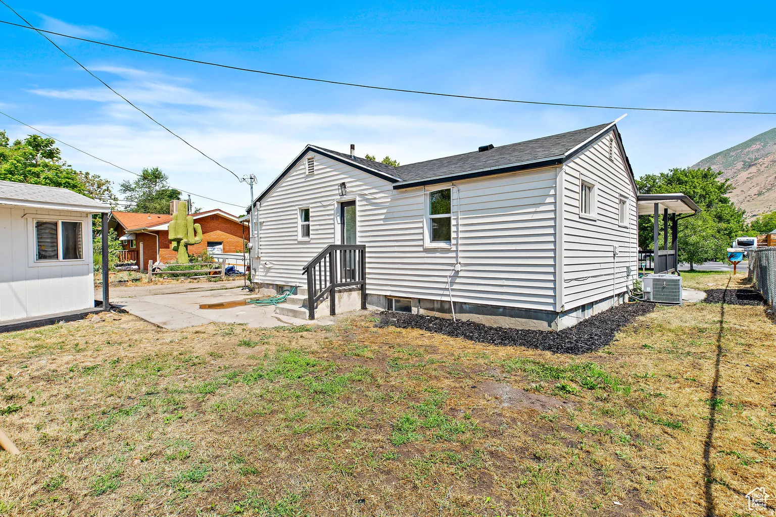White siding exterior with a dark shingle roof, a rear entry door, and a concrete patio