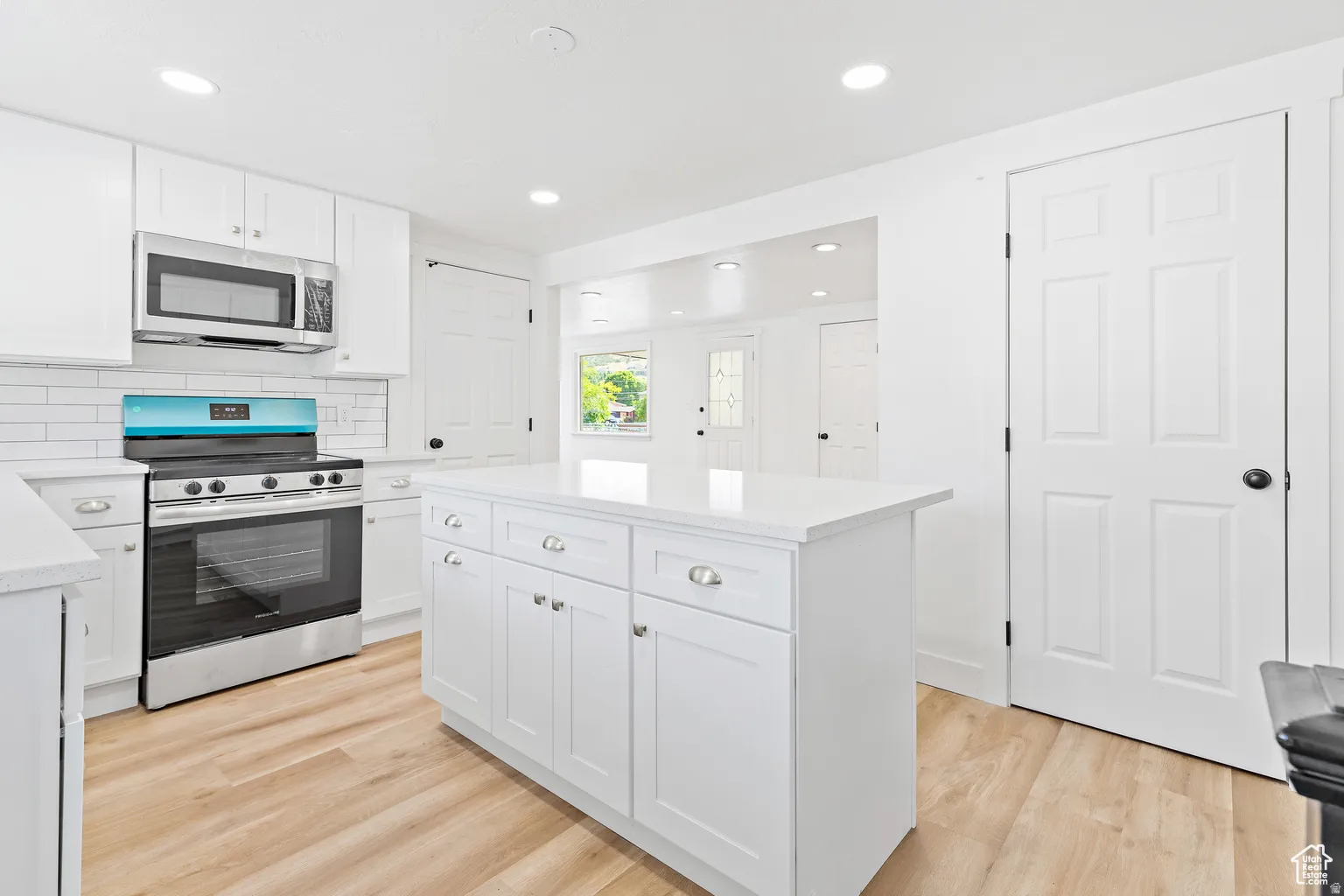 White cabinetry with silver hardware, white countertops, stainless steel appliances, white subway tile backsplash, and wood-finish flooring