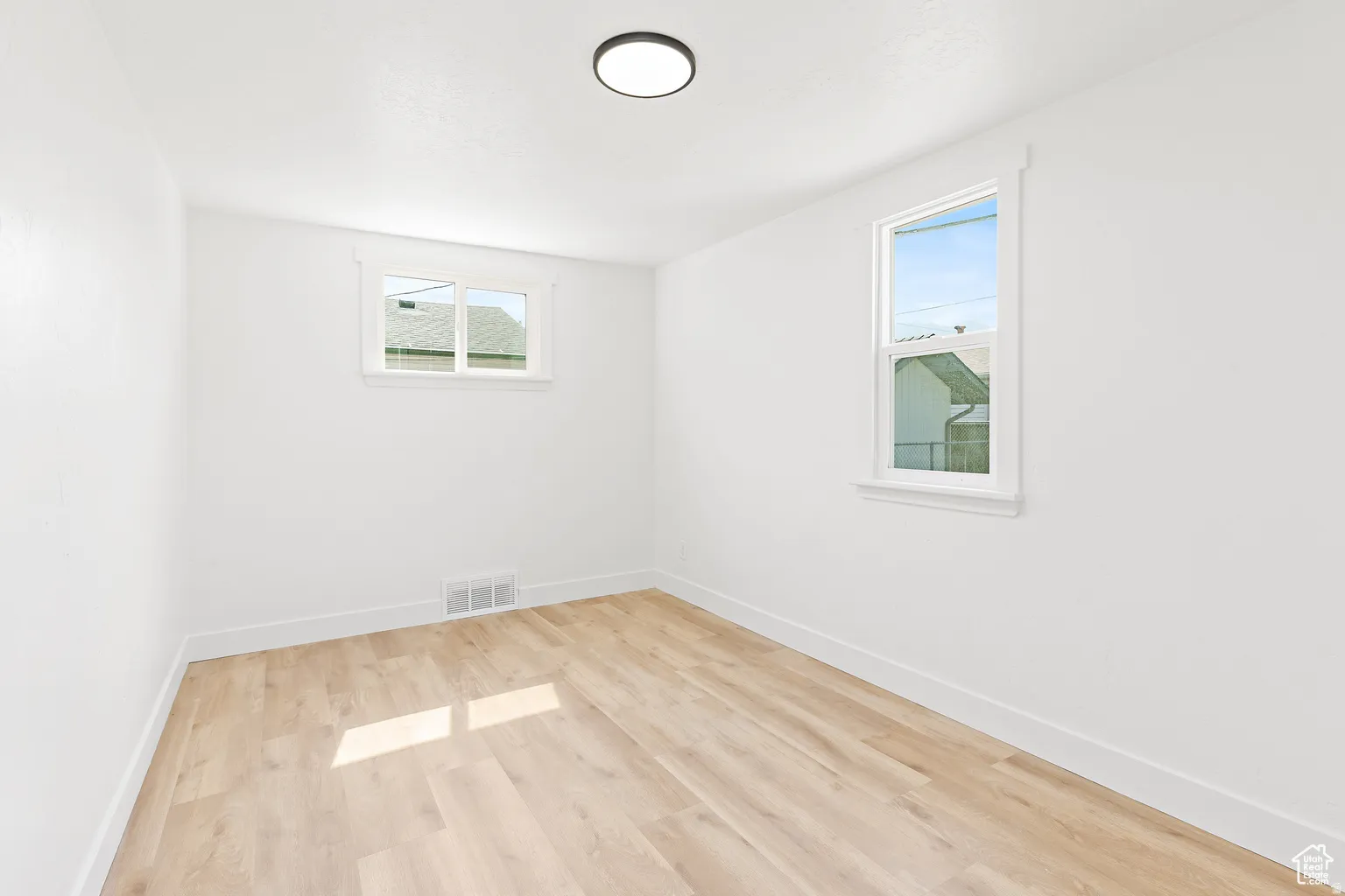 Wood-finish flooring, white walls, two windows, and a flush-mount ceiling light