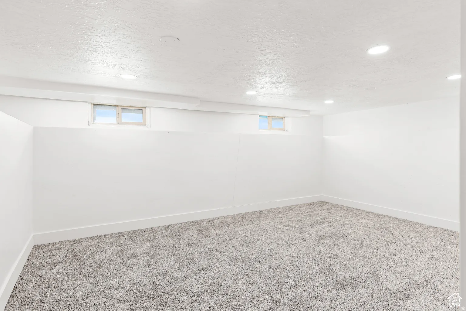 Recessed lighting illuminates this room, featuring light gray carpeting and white walls