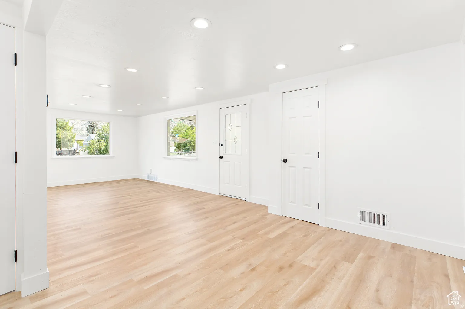 Bright open room featuring light wood-finish flooring, recessed ceiling lights, and multiple windows