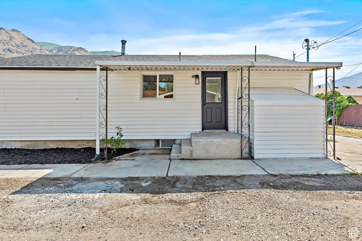 White horizontal siding exterior with a black entry door, covered porch, concrete steps, and a mountain backdrop