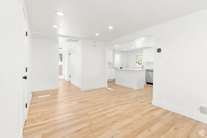 Open-concept living area featuring light wood-finish flooring, recessed ceiling lighting, and a kitchen with white cabinetry, stainless steel appliances, and a central island