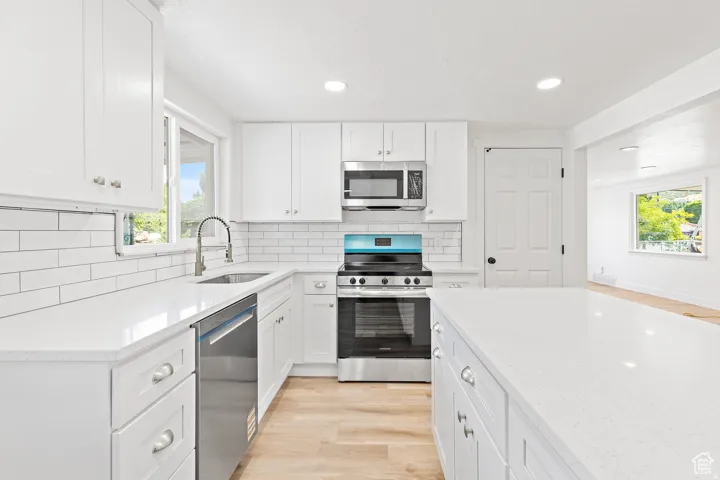 White cabinetry, stainless steel appliances, white subway tile backsplash, white countertops, and wood-finish flooring