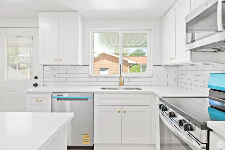 White shaker cabinetry, stainless steel appliances, subway tile backsplash, white countertops, and a stainless steel sink with gold-finish faucet