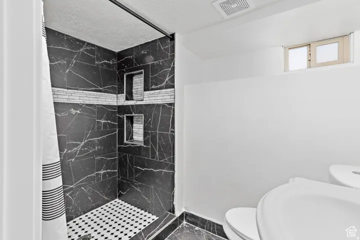 Shower featuring black marble-style tile walls, a decorative tile accent band, two recessed niches, and a black and white mosaic tile floor