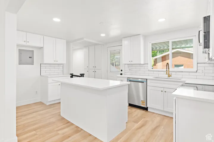 White shaker cabinetry, wood-finish flooring, white solid surface countertops, subway tile backsplash, and a stainless steel dishwasher
