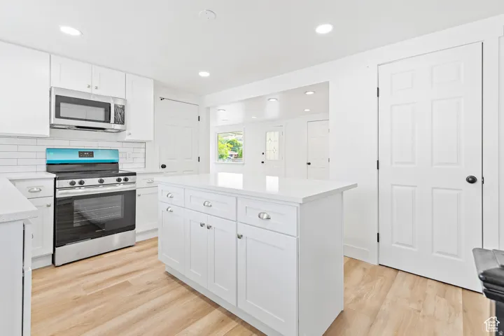 White cabinetry with silver hardware, white countertops, stainless steel appliances, white subway tile backsplash, and wood-finish flooring
