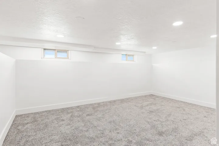 Recessed lighting illuminates this room, featuring light gray carpeting and white walls
