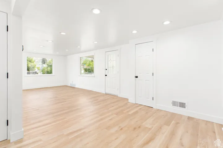 Bright open room featuring light wood-finish flooring, recessed ceiling lights, and multiple windows