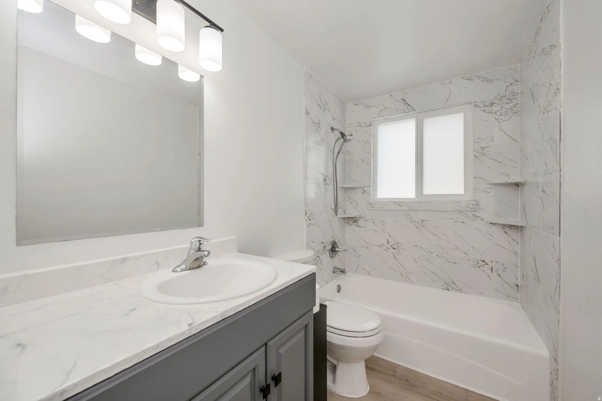 New  vanity with integrated sink and chrome faucet, vanity lighting, wall-mounted mirror, white bathtub, and new white-veined wall tiling