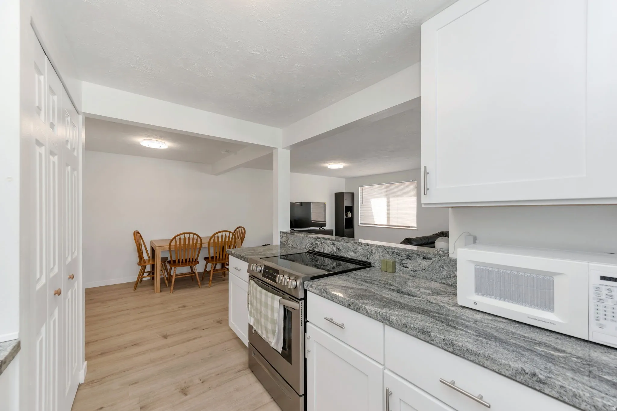 Kitchen featuring white cabinetry, granite countertops, a stainless steel range, and wood-finish LVP flooring