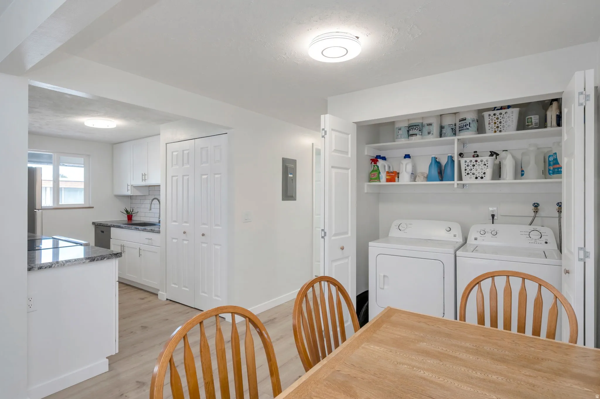 Laundry closet with stacked shelving and white appliances, featuring light