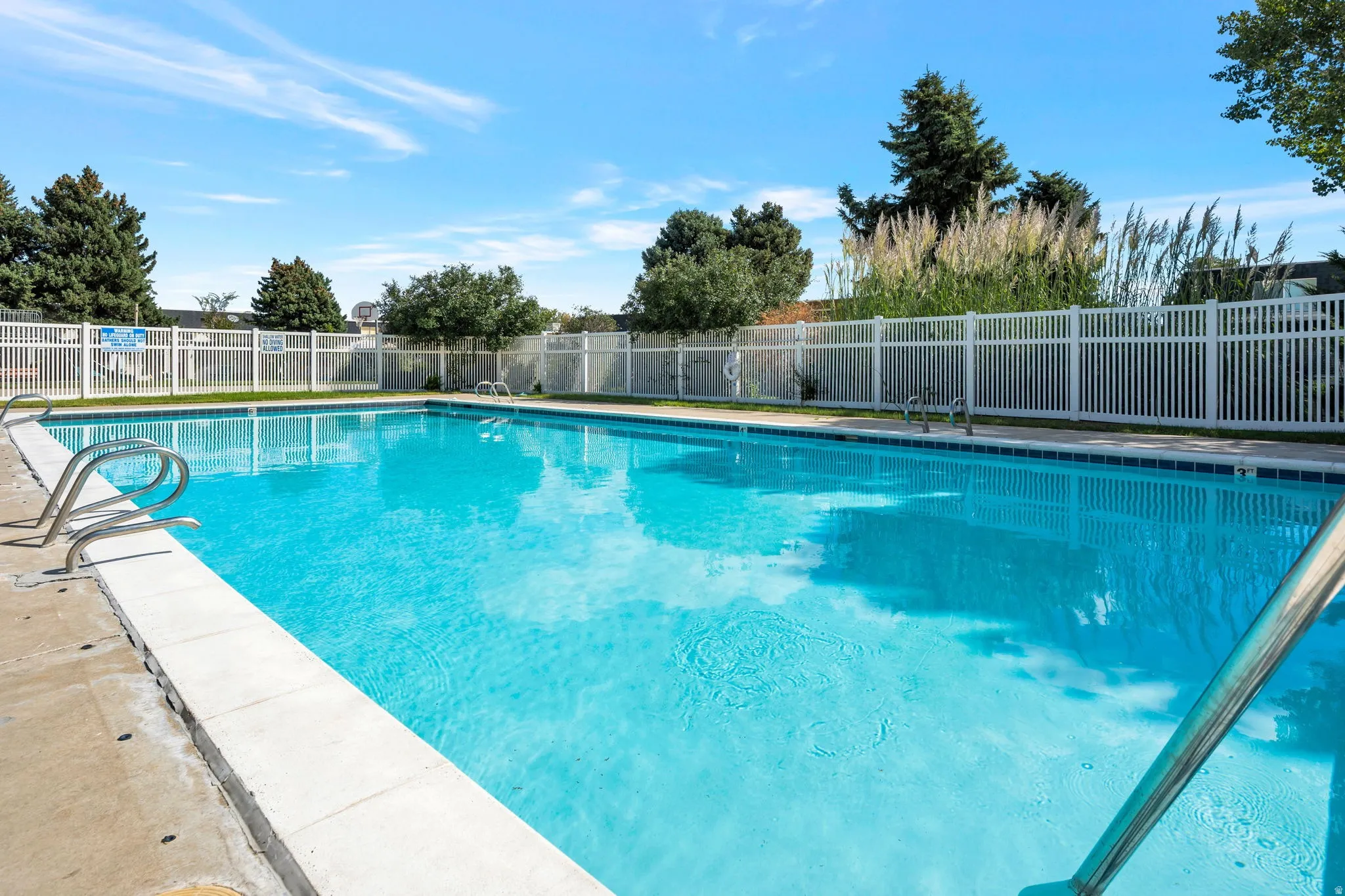 Expansive outdoor swimming pool featuring a concrete surround, white fencing, and integrated pool ladders