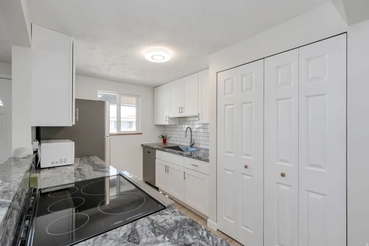 Kitchen featuring new cabinetry, a new granite countertop, a white subway tile backsplash, a stainless steel refrigerator, and a built-in electric range