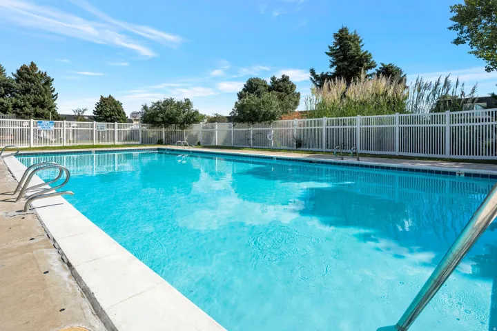 Expansive outdoor swimming pool featuring a concrete surround, white fencing, and integrated pool ladders
