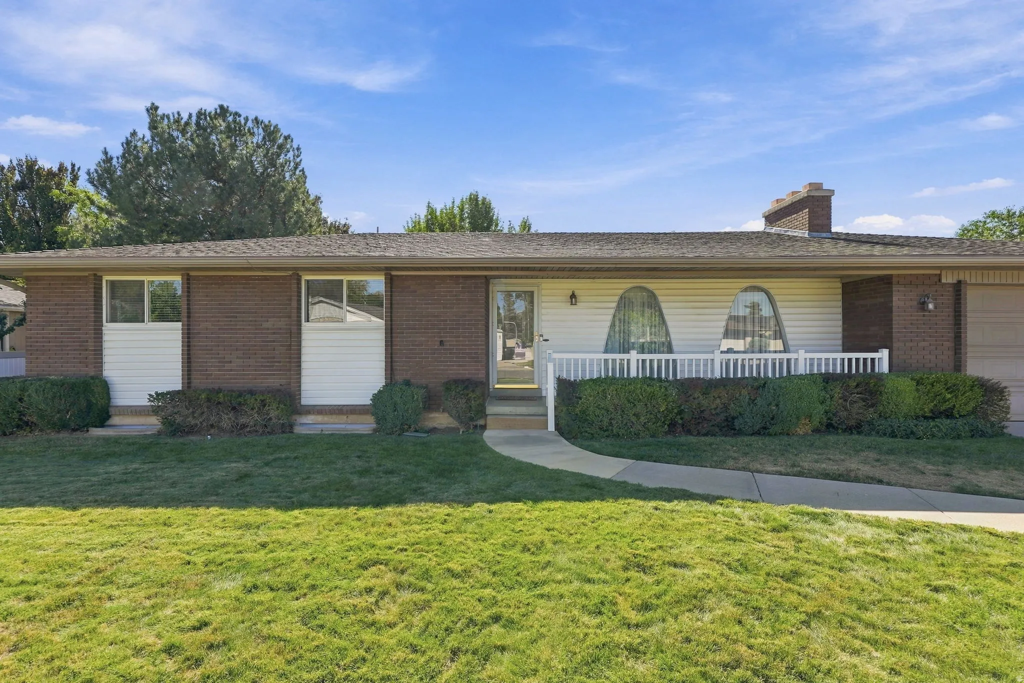 Brick facade, white siding, curved front windows, white railing, paved walkway
