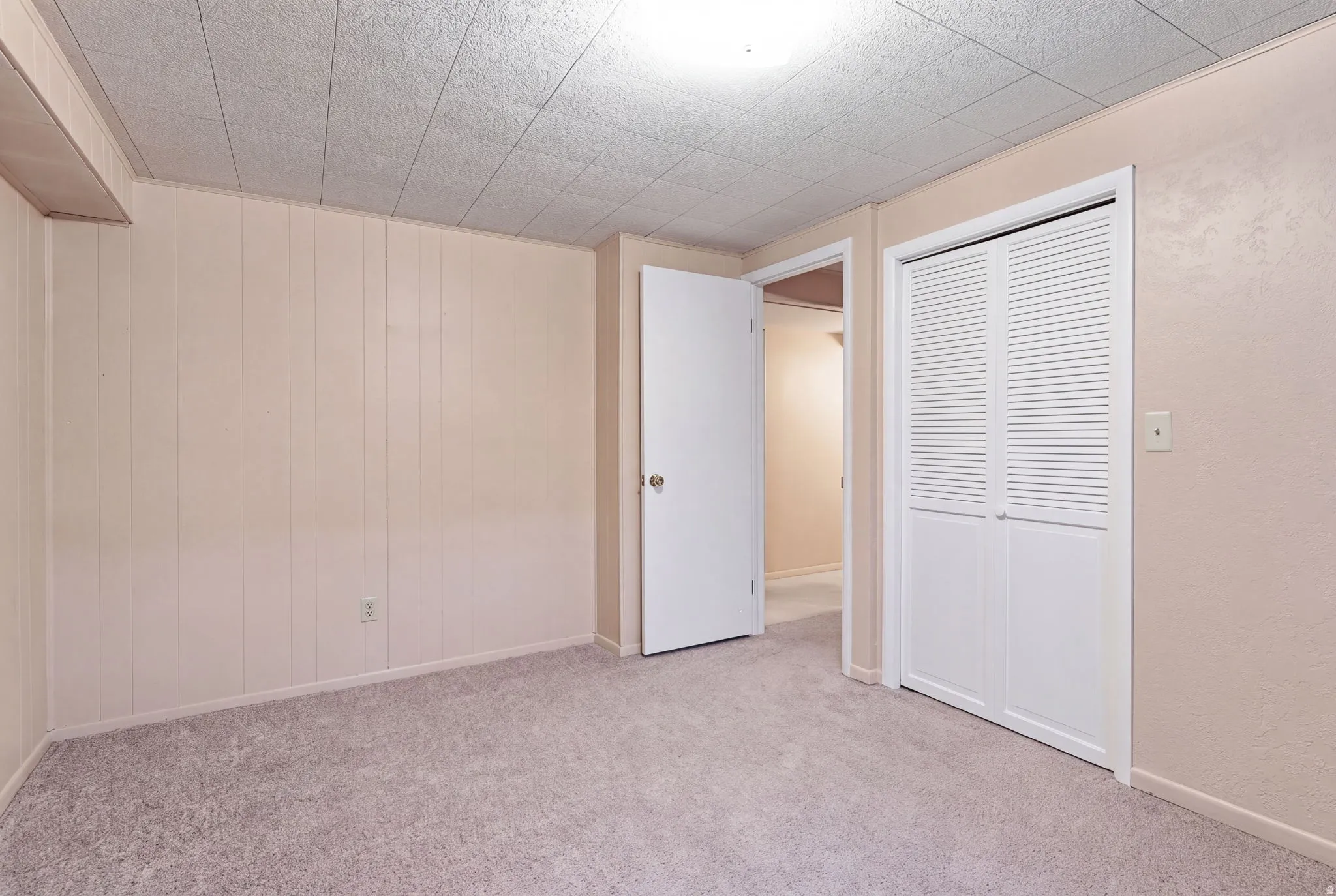 Carpeted flooring, paneled wall detail, textured ceiling, louvered bi-fold closet doors, and interior door