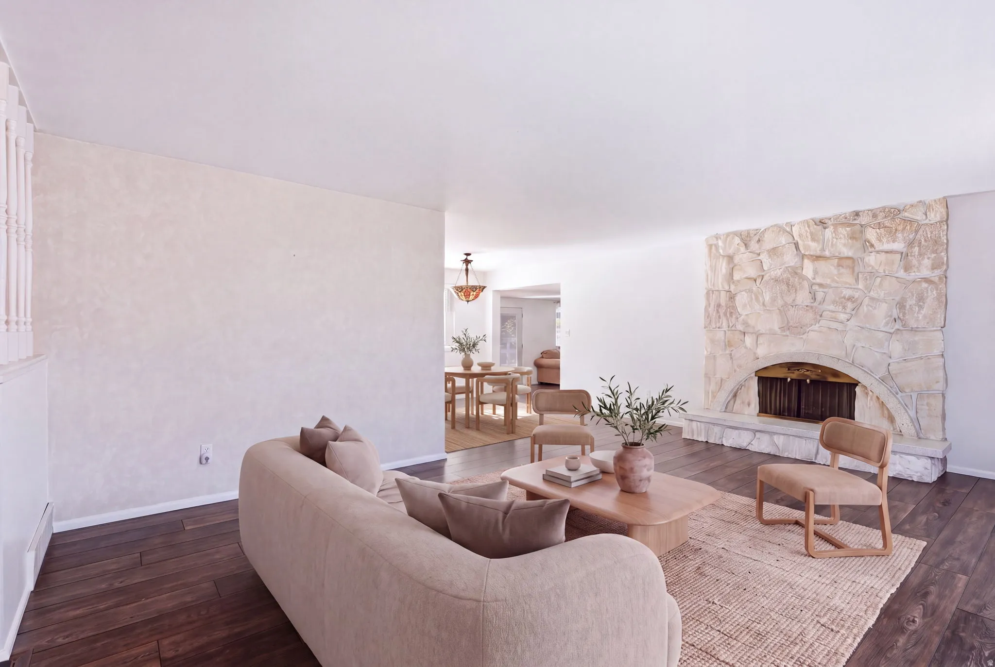 Stone fireplace with an arched firebox, dark wood-finish flooring, and white painted walls