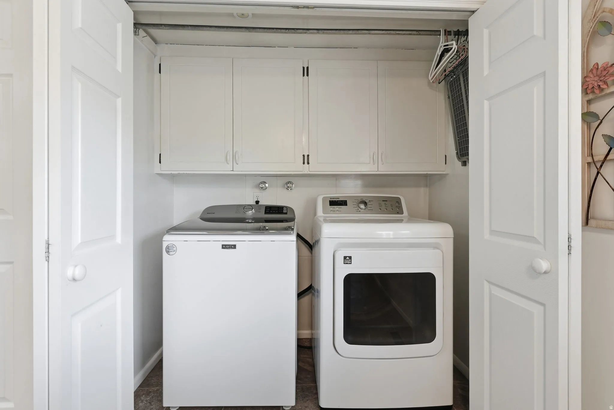 White bi-fold doors open to a utility area with upper cabinetry and a chrome hanging rod