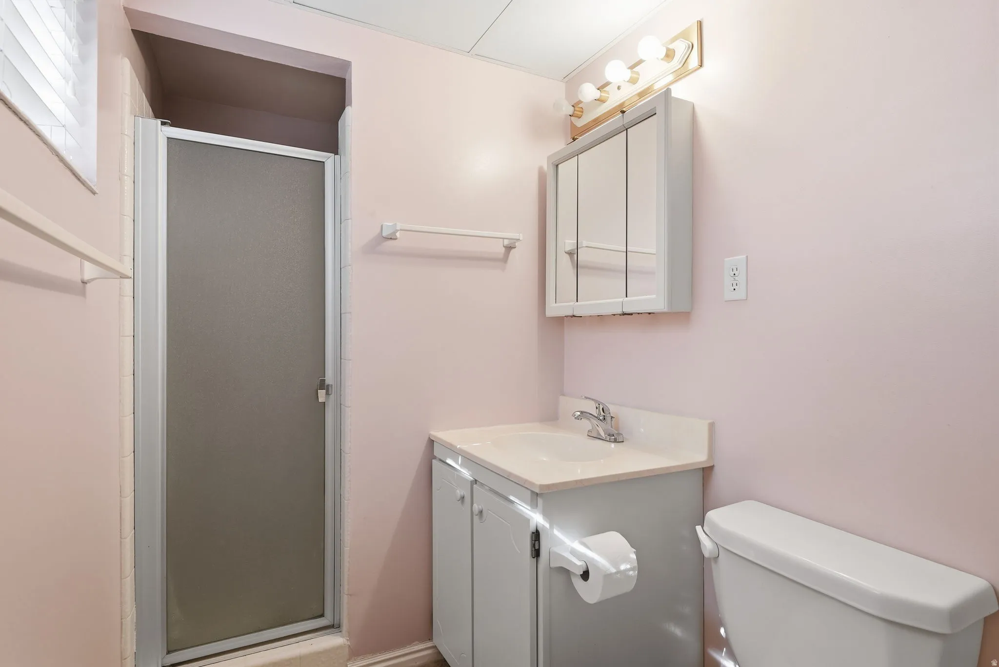 Enclosed shower with frosted glass, vanity with integrated sink, wall-mounted medicine cabinet, and overhead light fixture