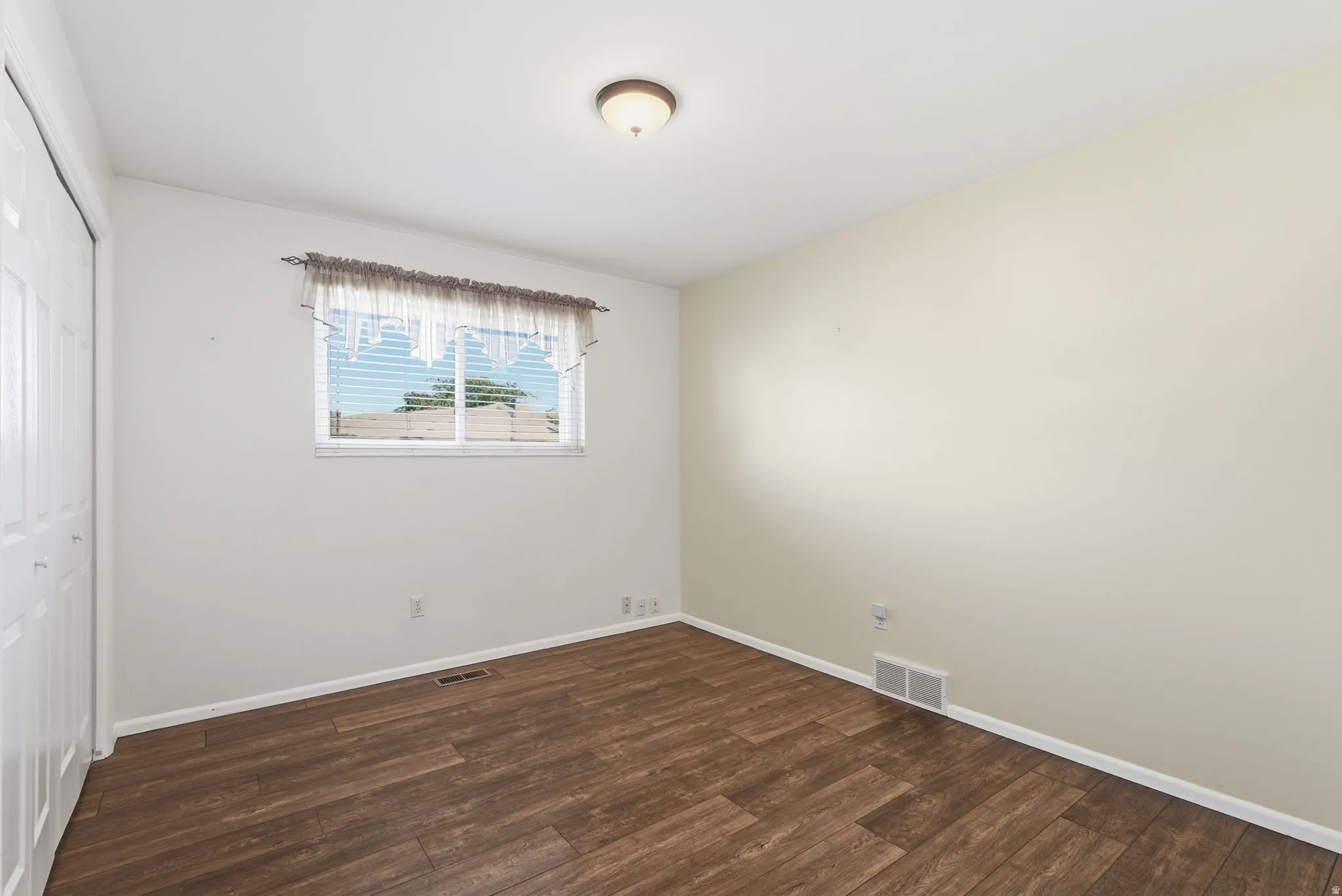 Wood-finish flooring, white bi-fold closet doors, single window, flush-mount ceiling light fixture, and light-toned walls