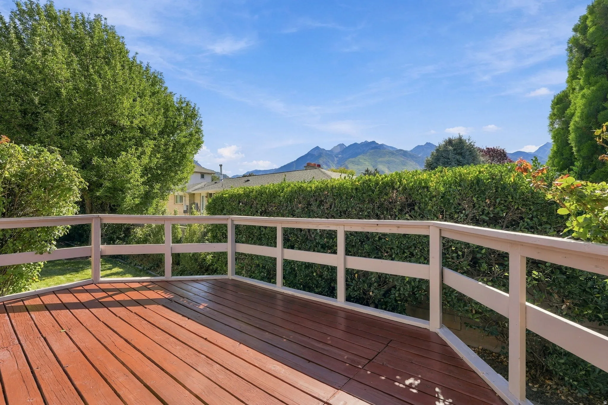 Expansive wood deck with white railing, surrounded by mature greenery, offering mountain scenery