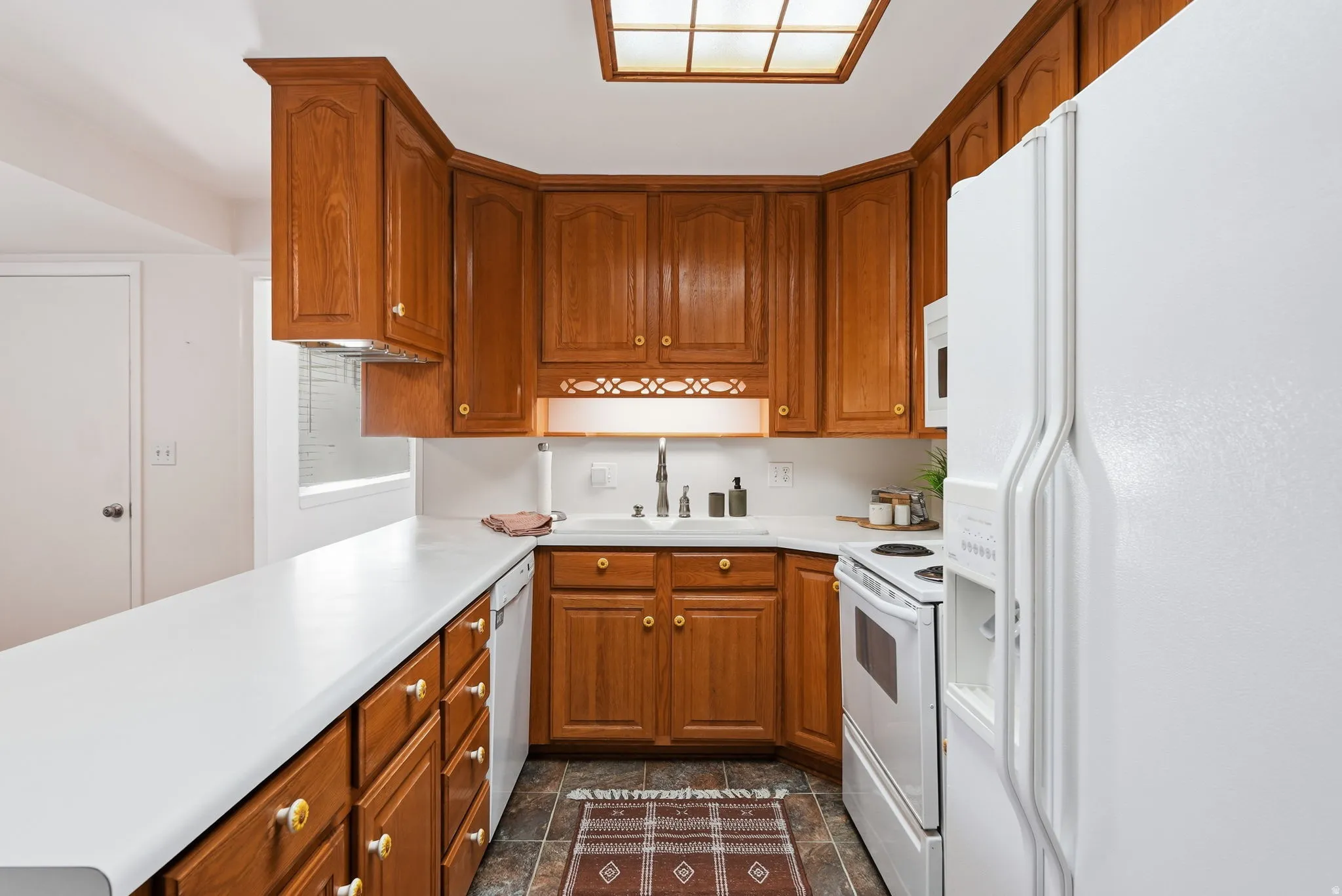 Wood-finish cabinetry, white countertops, built-in dishwasher, and white refrigerator