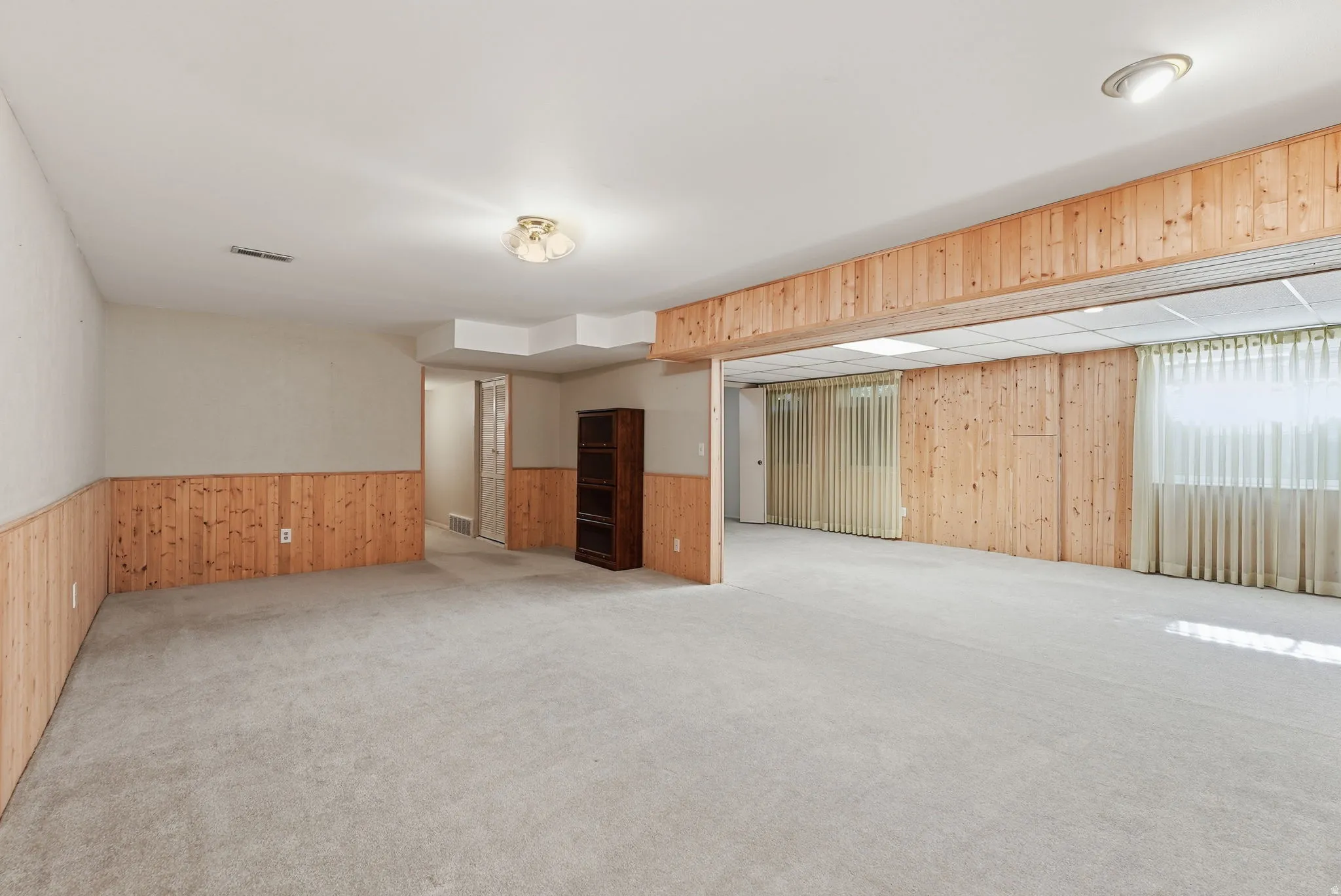 Expansive room featuring light-toned carpeting and wood paneling