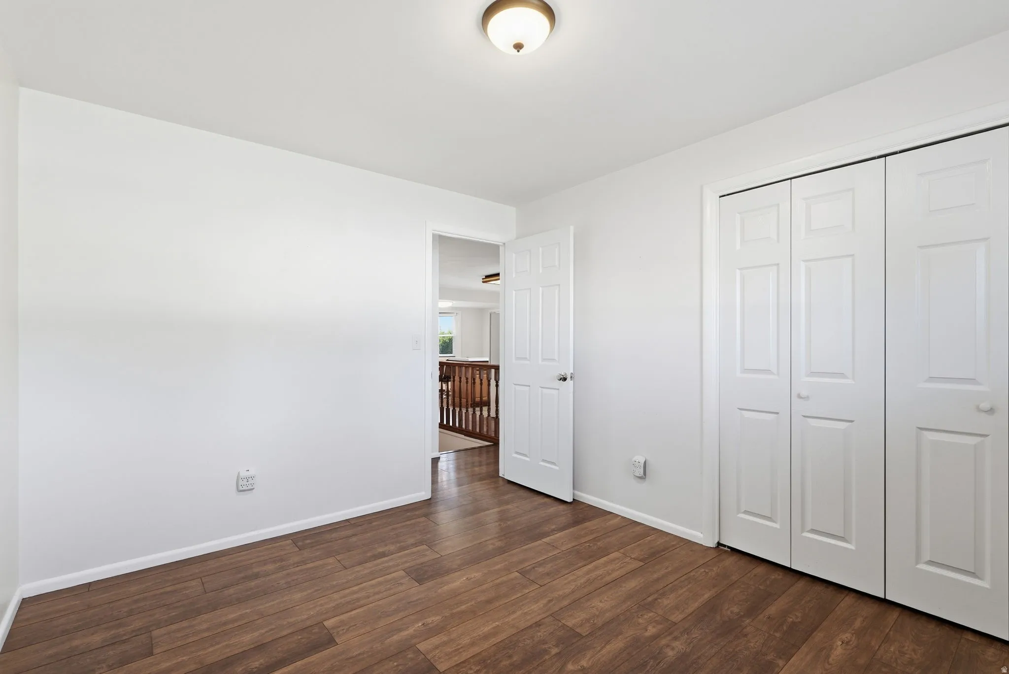 Wood-finish flooring, white walls, white trim, bifold closet doors, and a ceiling-mounted light fixture