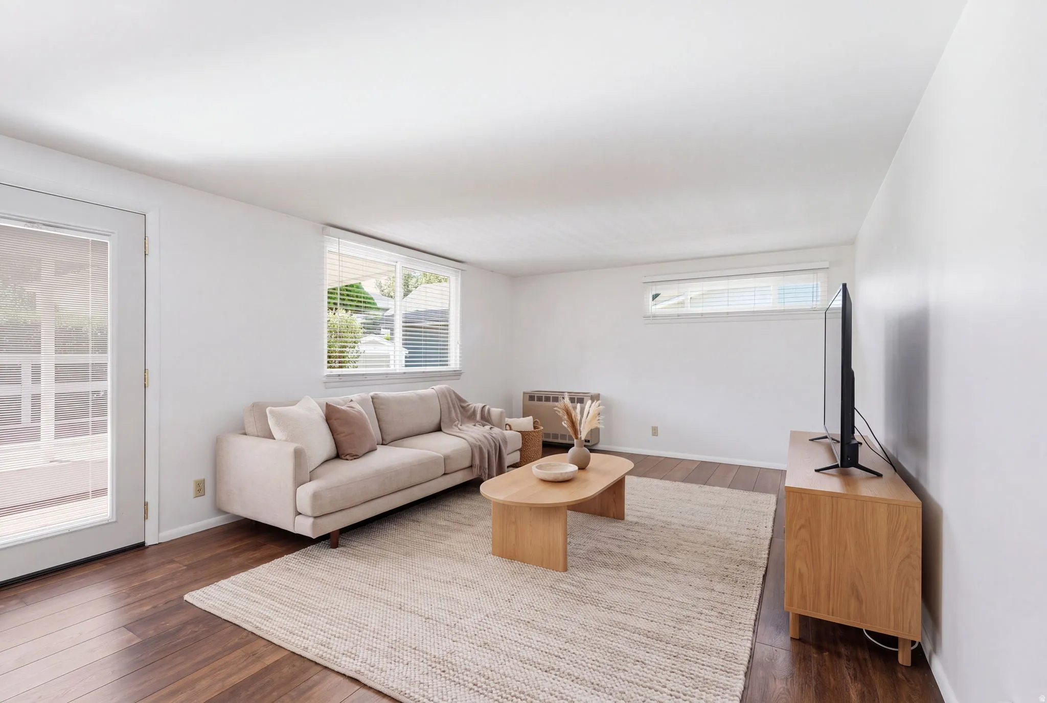 Wood-finish flooring, white walls, multiple windows with blinds, and glass-paneled door