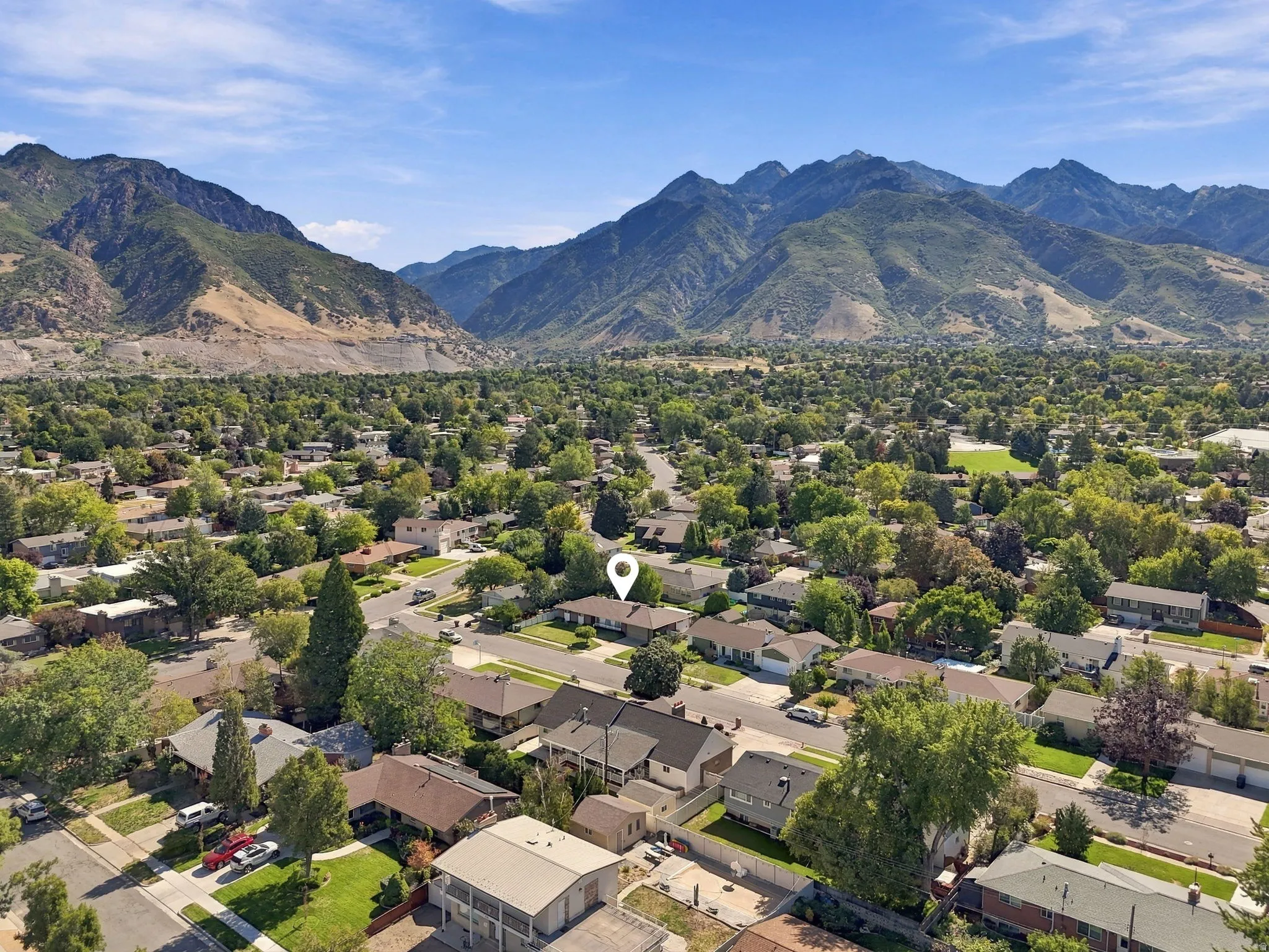 Mountainous terrain backdrop, residential streets, lush tree canopy, scattered rooftops, clear blue sky