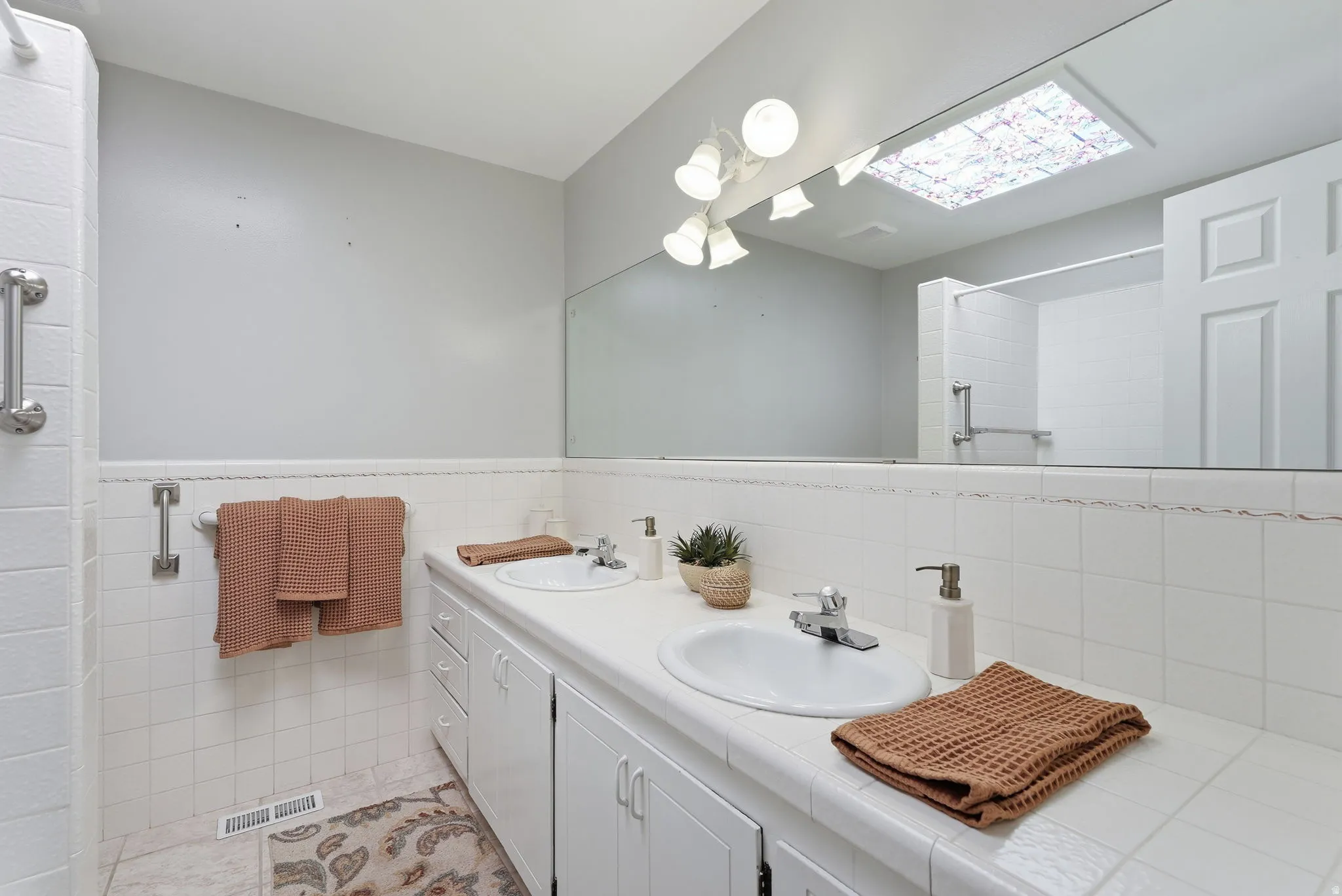 Dual vanity with integrated sinks, white tile countertop, white cabinetry, and wall-mounted mirror
