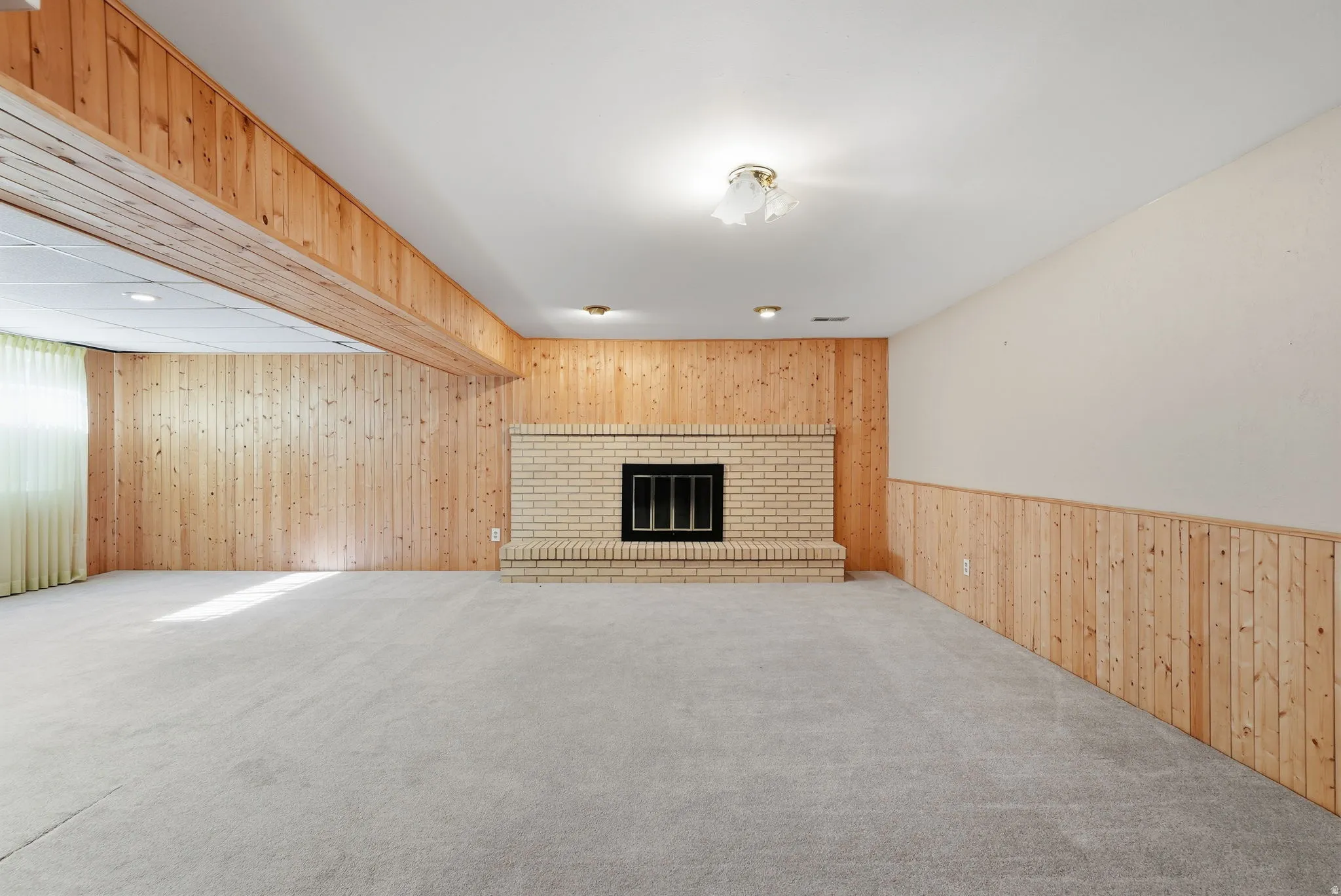 Recessed lighting, light-colored carpet, wood paneling, and a brick fireplace with a black insert