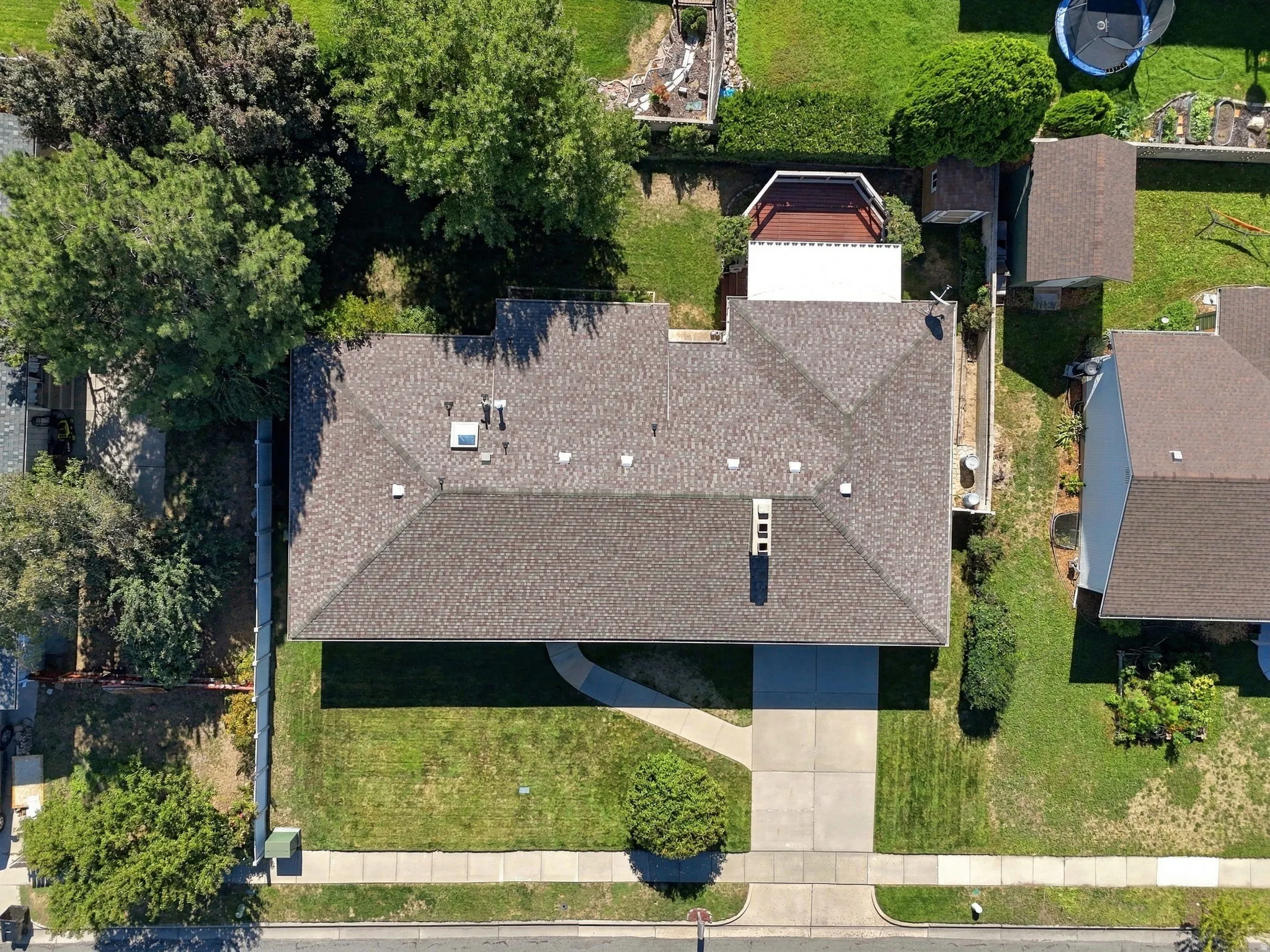 Gable roofline with asphalt shingles, concrete driveway, front yard with mature landscaping, and an additional storage shed