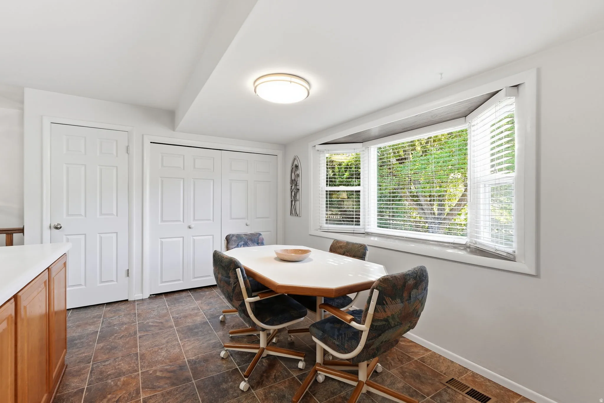 Bay window with blinds, dual bi-fold closet doors, tile flooring, and light wood-finish cabinetry