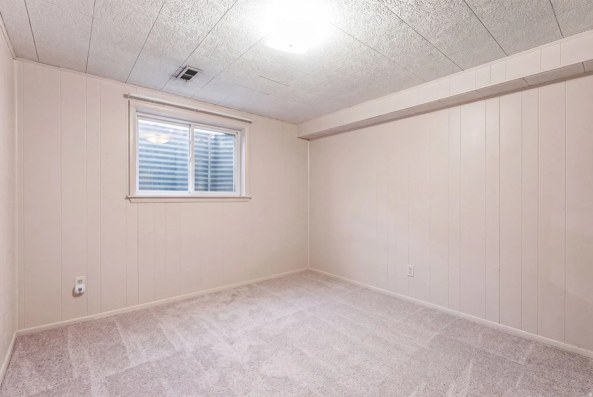 Recessed window with horizontal blinds, textured ceiling, wall paneling, and carpeted flooring
