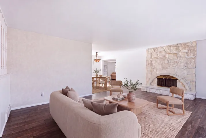 Stone fireplace with an arched firebox, dark wood-finish flooring, and white painted walls
