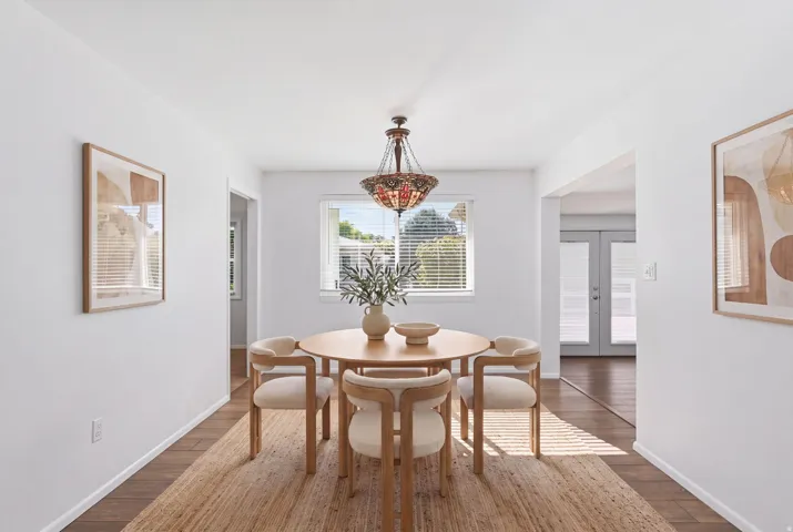 Wood-finish flooring with an area rug, white walls, and a decorative chandelier