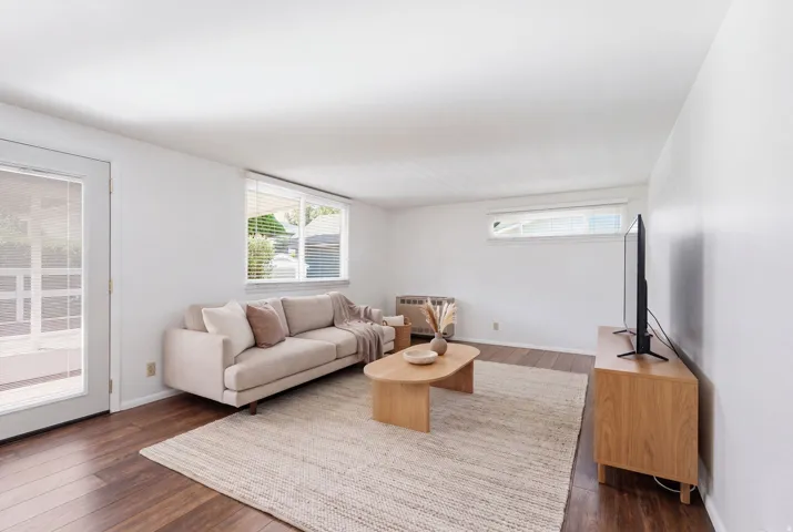 Wood-finish flooring, white walls, multiple windows with blinds, and glass-paneled door