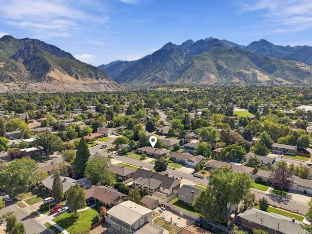 Mountainous terrain backdrop, residential streets, lush tree canopy, scattered rooftops, clear blue sky