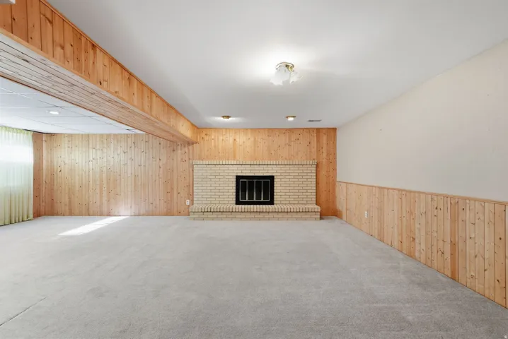 Recessed lighting, light-colored carpet, wood paneling, and a brick fireplace with a black insert