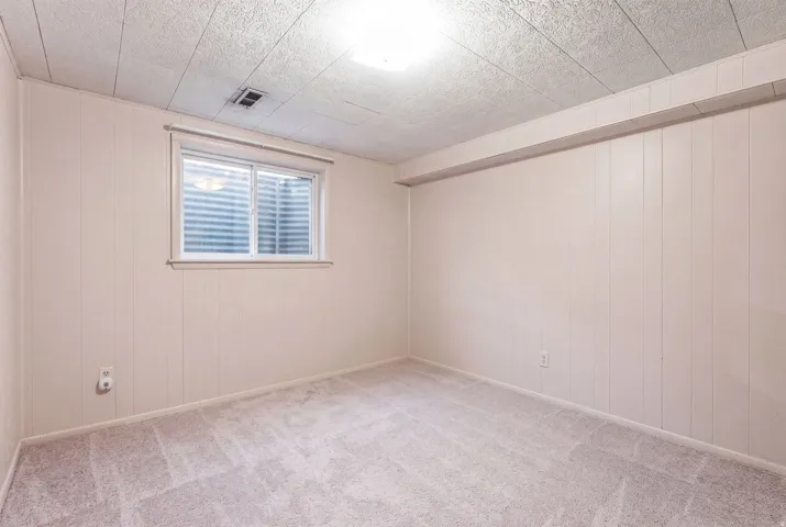 Recessed window with horizontal blinds, textured ceiling, wall paneling, and carpeted flooring