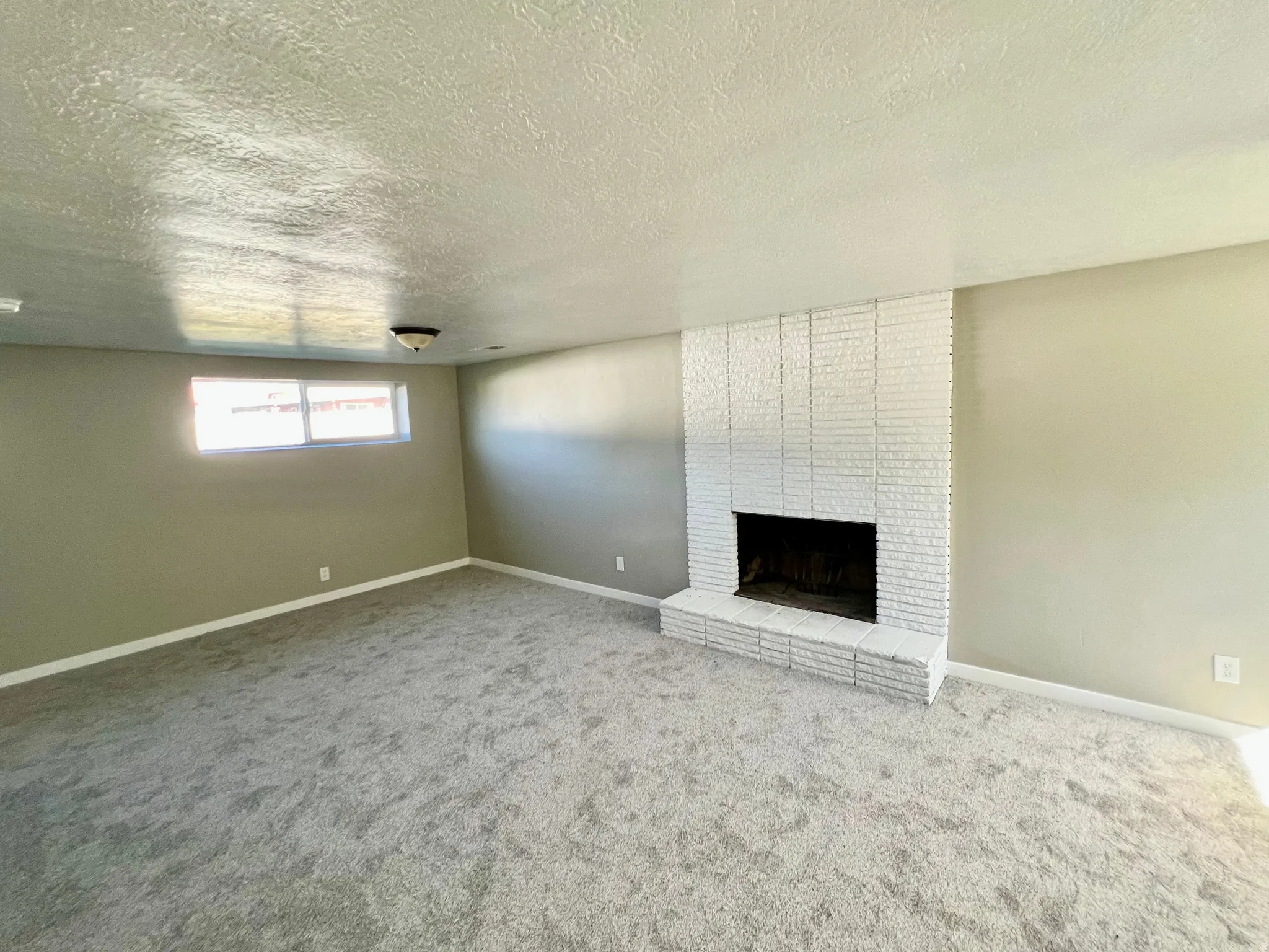 Expansive carpeted room featuring a white-painted brick fireplace and a horizontal window